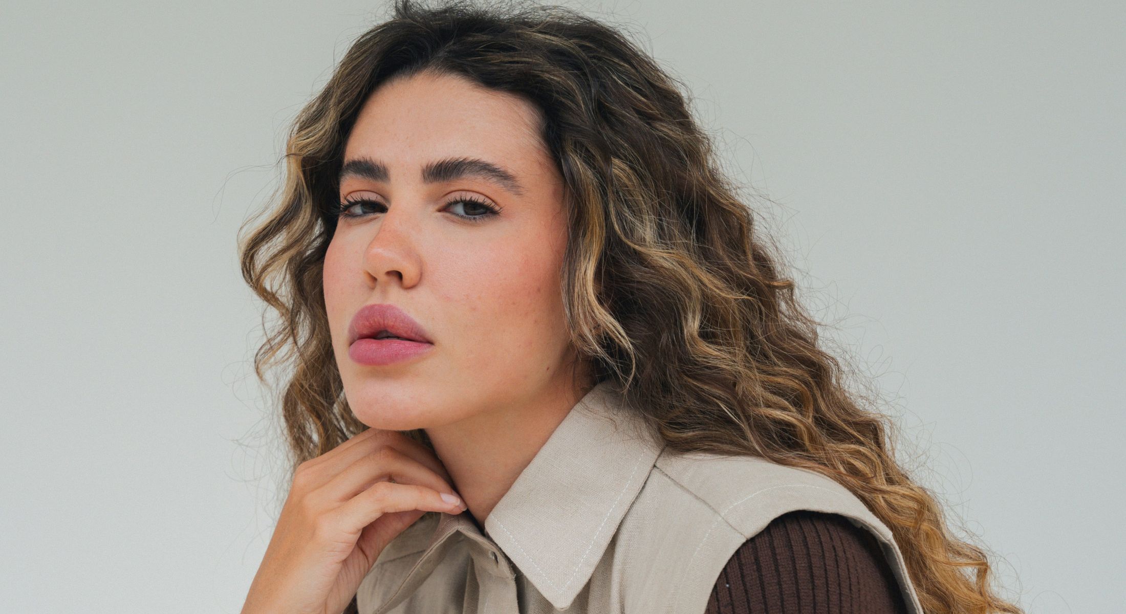 Woman with curly hair and neutral expression.