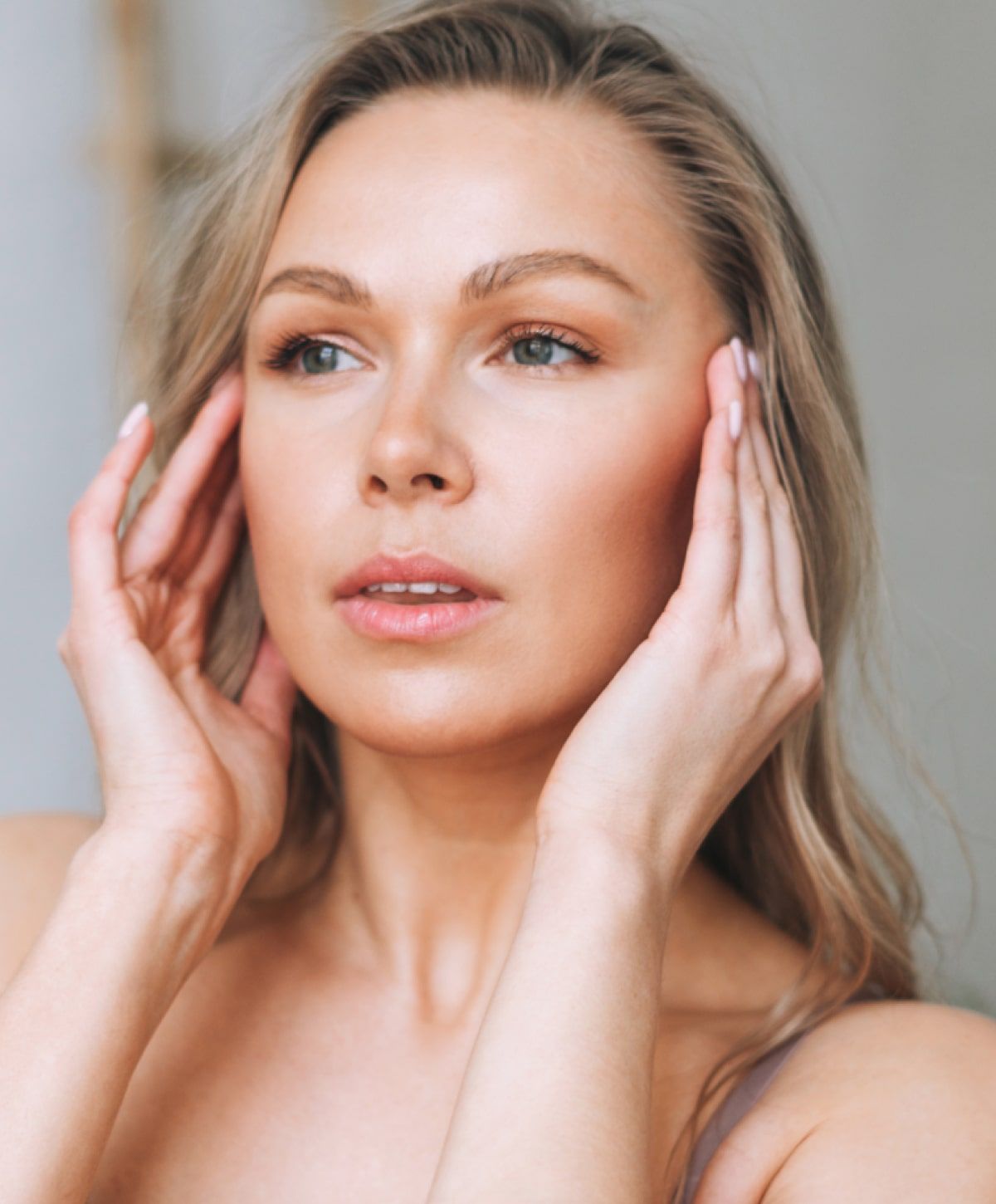 Woman gently touching her face with soft expression.